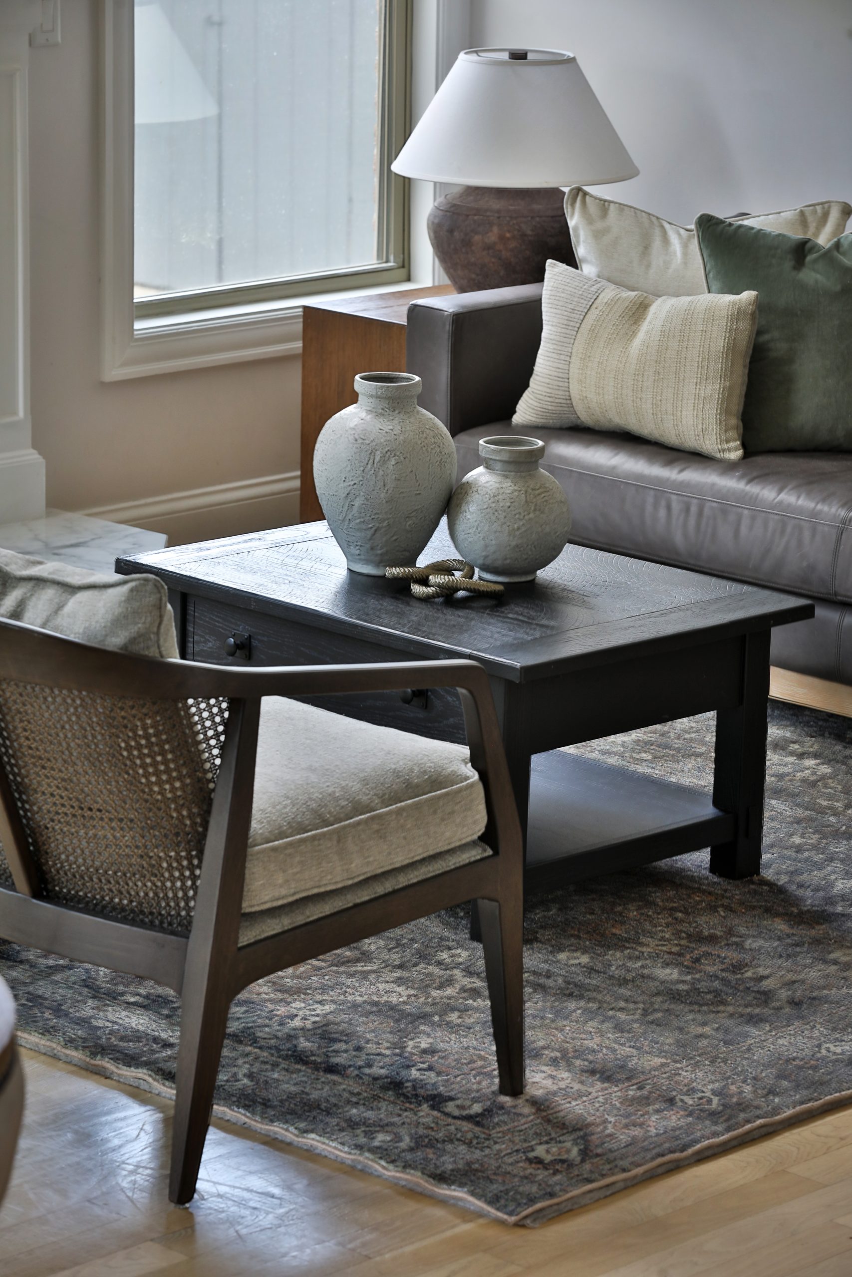 Cozy sitting area off the kitchen featuring the Jake Leather Sofa from Pottery Barn, caned-back accent chairs flanking a fireplace, and a warm-toned Amber Lewis x Loloi rug — tying together modern and collected elements in this open-concept home