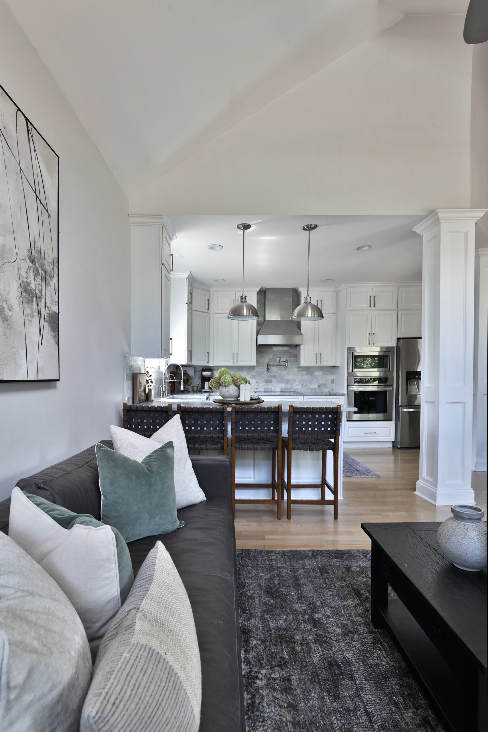 View from the living room into the kitchen, featuring a Jake Leather Sofa from Pottery Barn and black leather basket weave counter stools from World Market. The space is grounded by an Amber Lewis x Loloi area rug, tying together the warm, modern design elements throughout the open-concept layout.