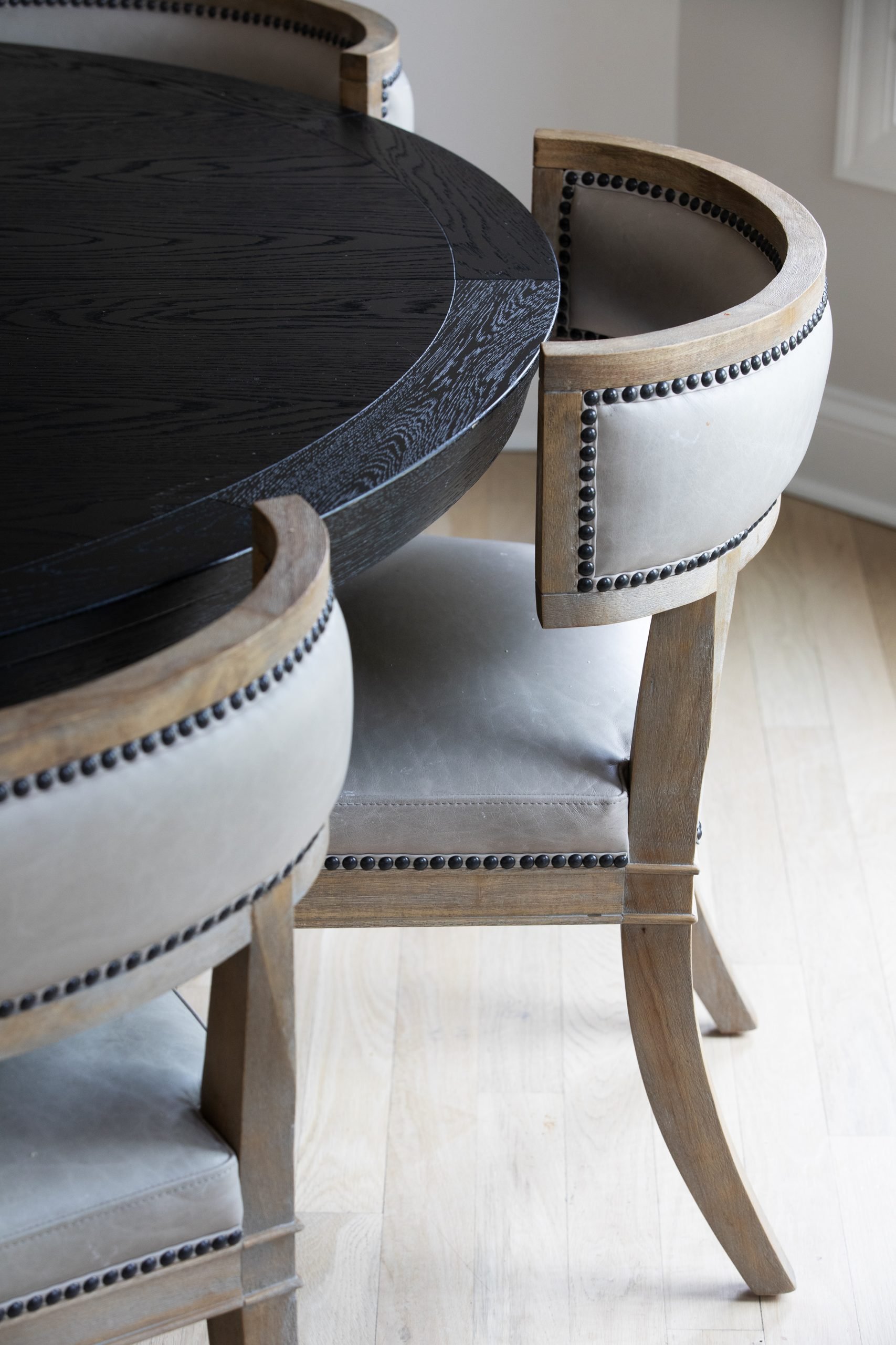Close-up of the Carter Dining Chair, featuring a curved back and dark nailhead detailing that complement the black round dining table from Arhaus. The textures and tones create a refined, cohesive dining space.