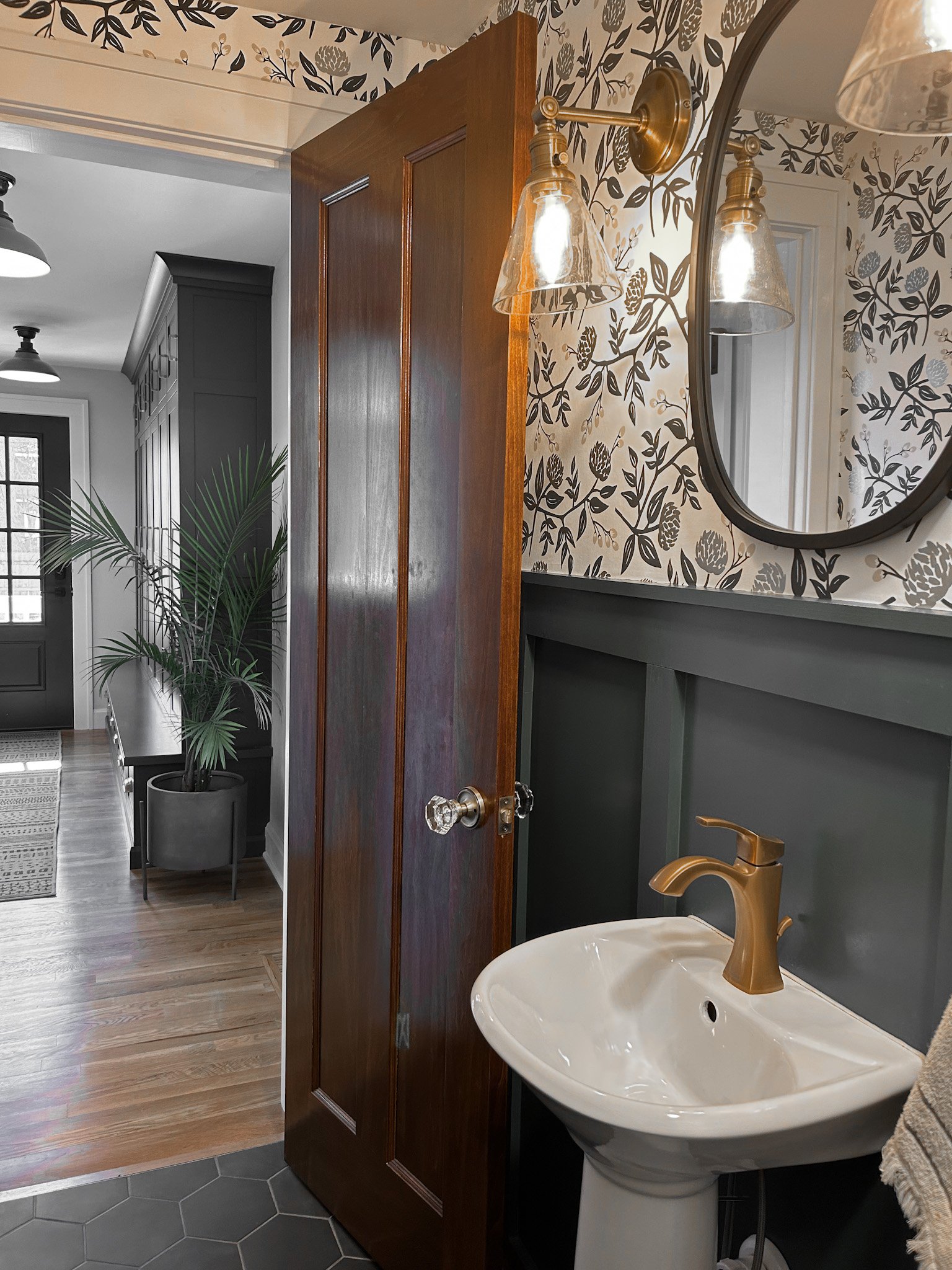 Classic bathroom with modern twist featuring ornate floral wallpaper, wainscoting and wall mounted mirror.