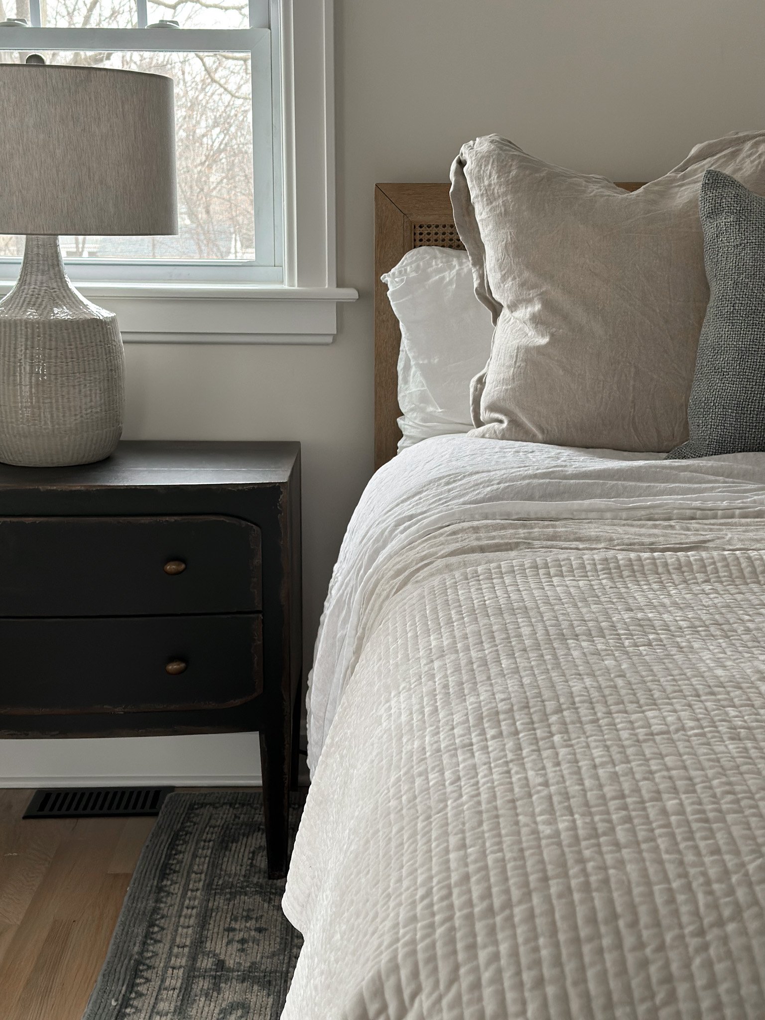 Bedroom interior design finished look with neutral toned bedding, ceramic table lamp and vintage night stands.