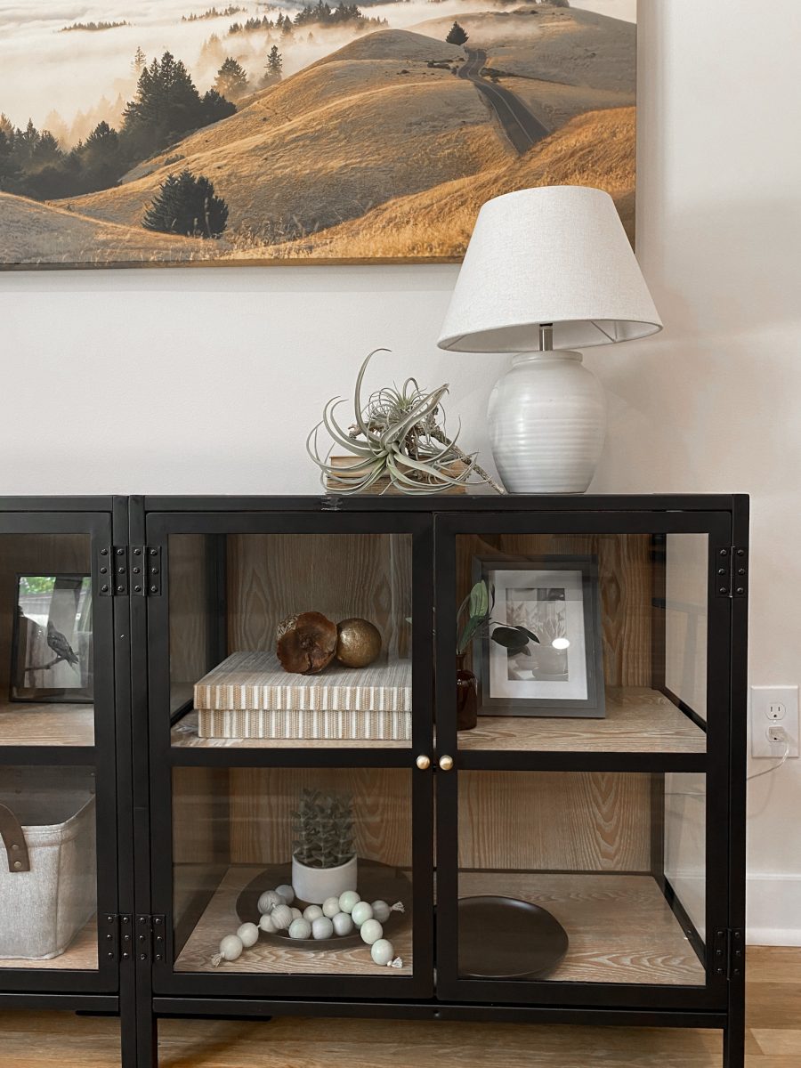 A modern console decorated with modern lamps, faux greenery, large prints and woven baskets.