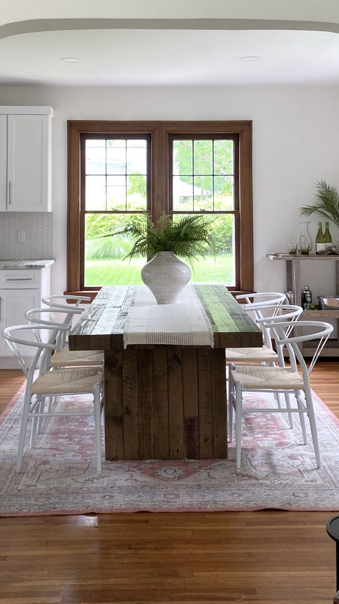 Dining room staging with natural wood dining table, modern wicker chairs and ornate vase.
