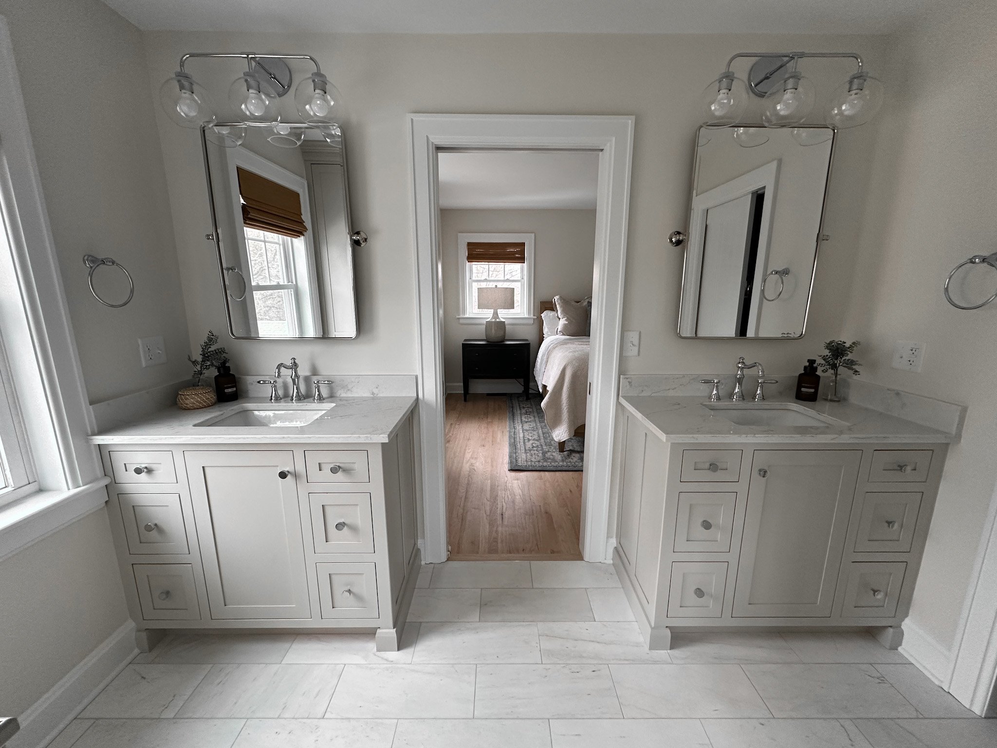 Large custom remodeled bathroom with double vanity, sconce lighting and white tile flooring.
