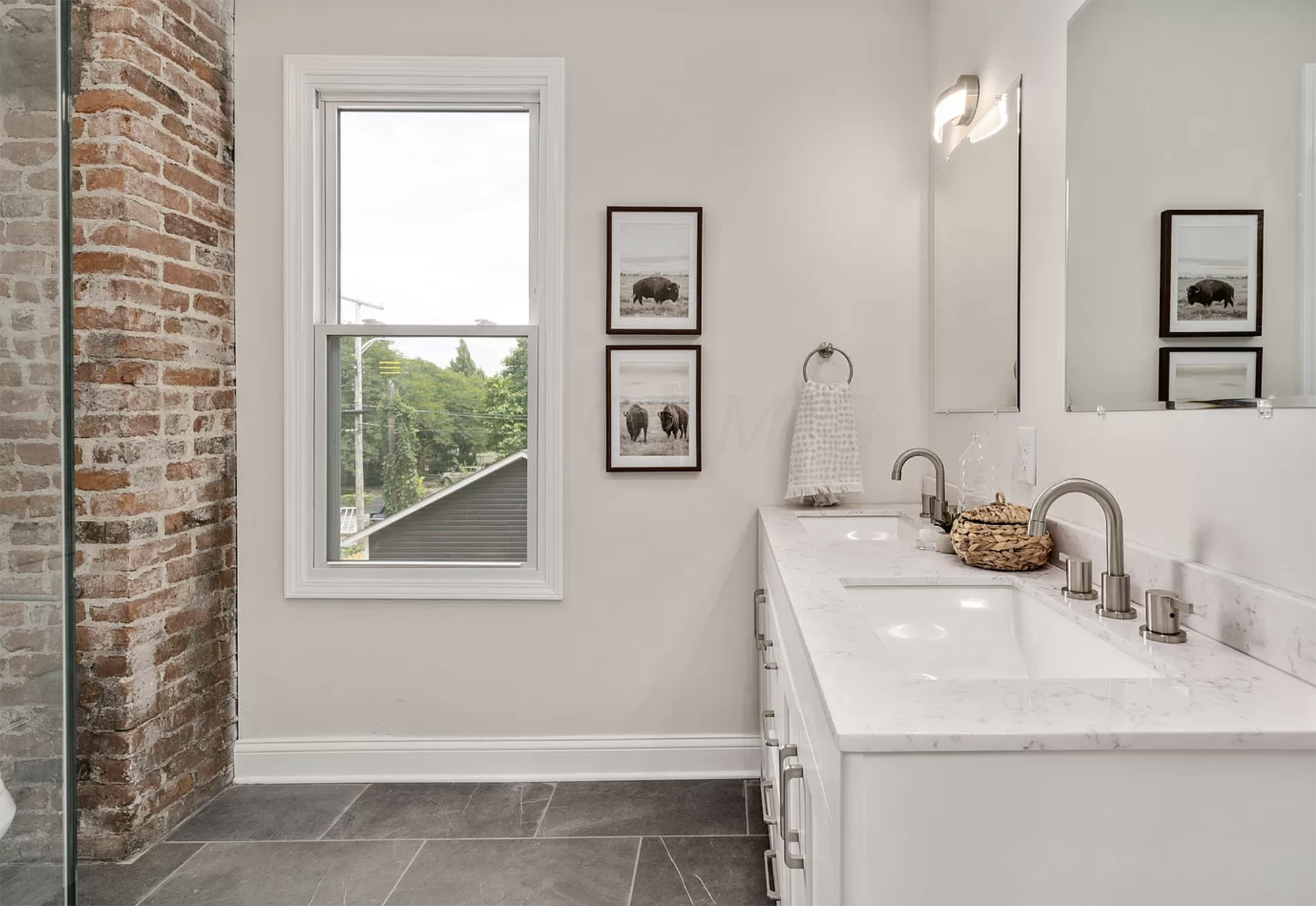 Double vanity decorated with woven baskets, hand towels and framed artwork.