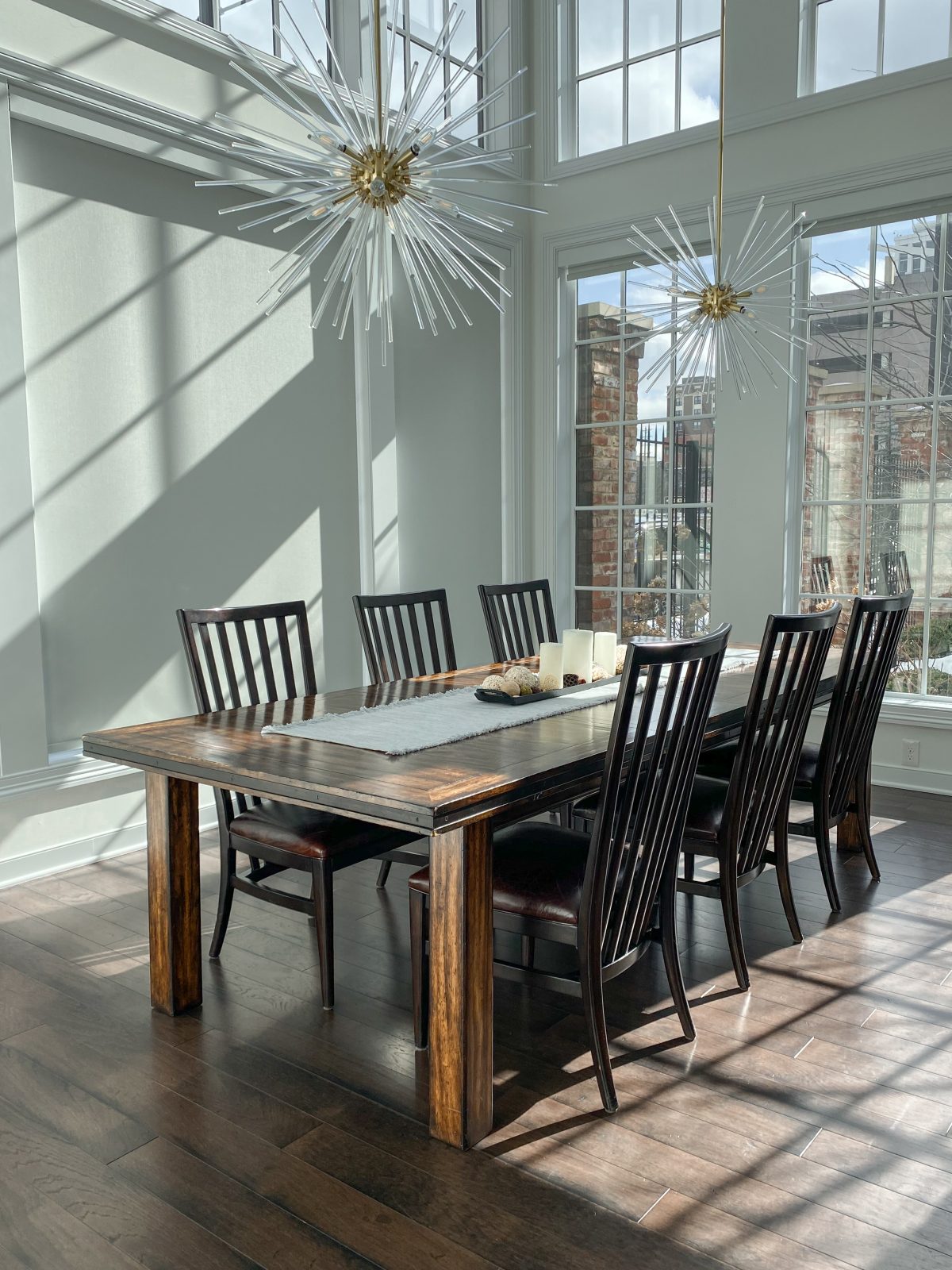 Luxury dining room with large windows, high ceilings, modern chandeliers and dark stained dining table.