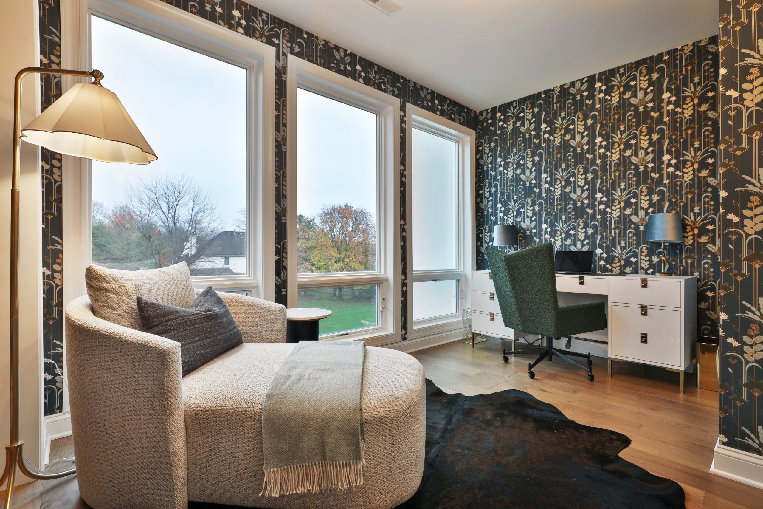 At home office space with ornate wallpaper, chaise lounge chair and warm lighting overlooking a country club gold course in luxury condo.