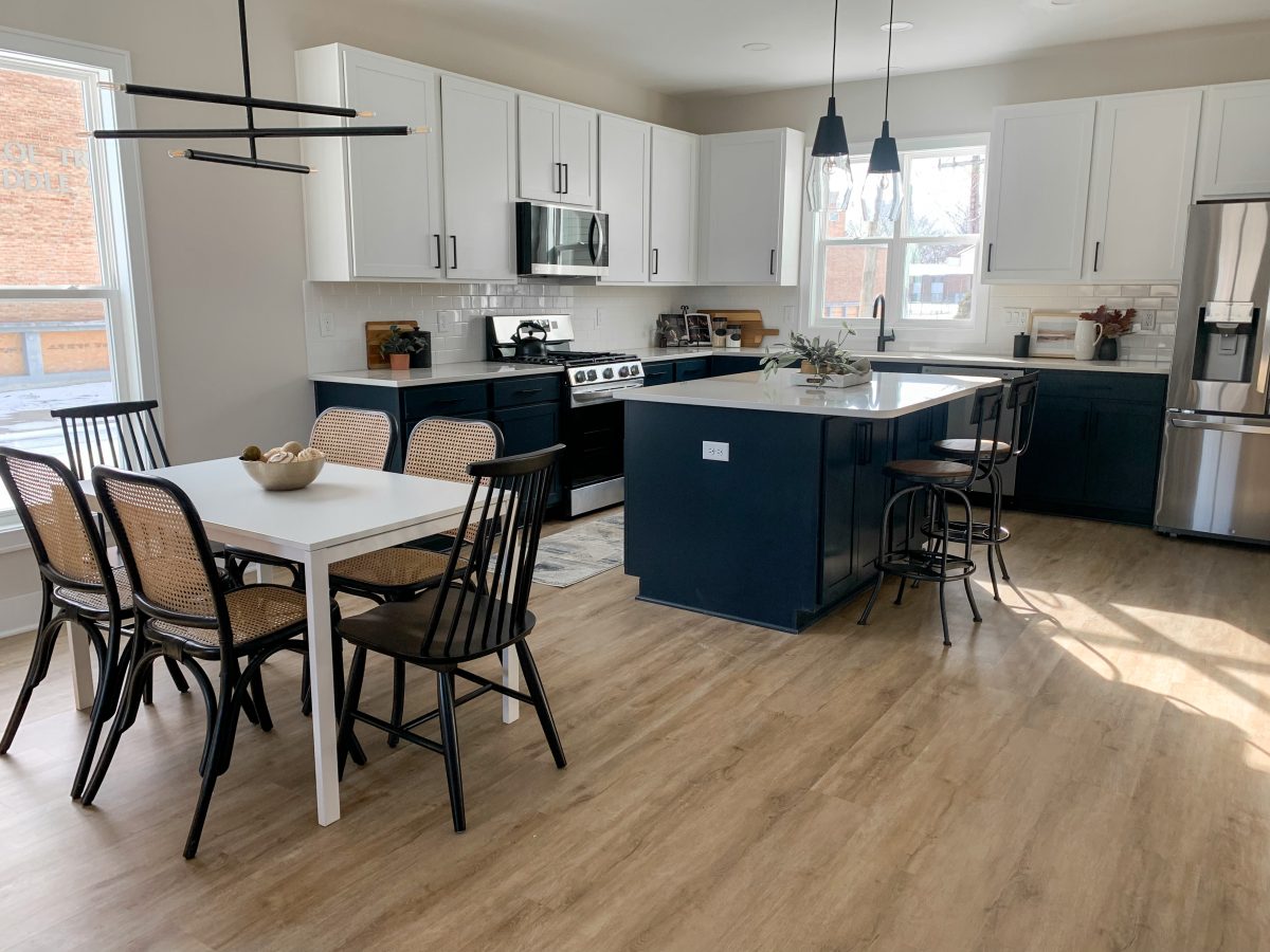 An open floor-plan kitchen with black cabinets, white solid surface countertops, stainless appliances and classic kitchenette dining area in downtown Pacific Palisades, California.