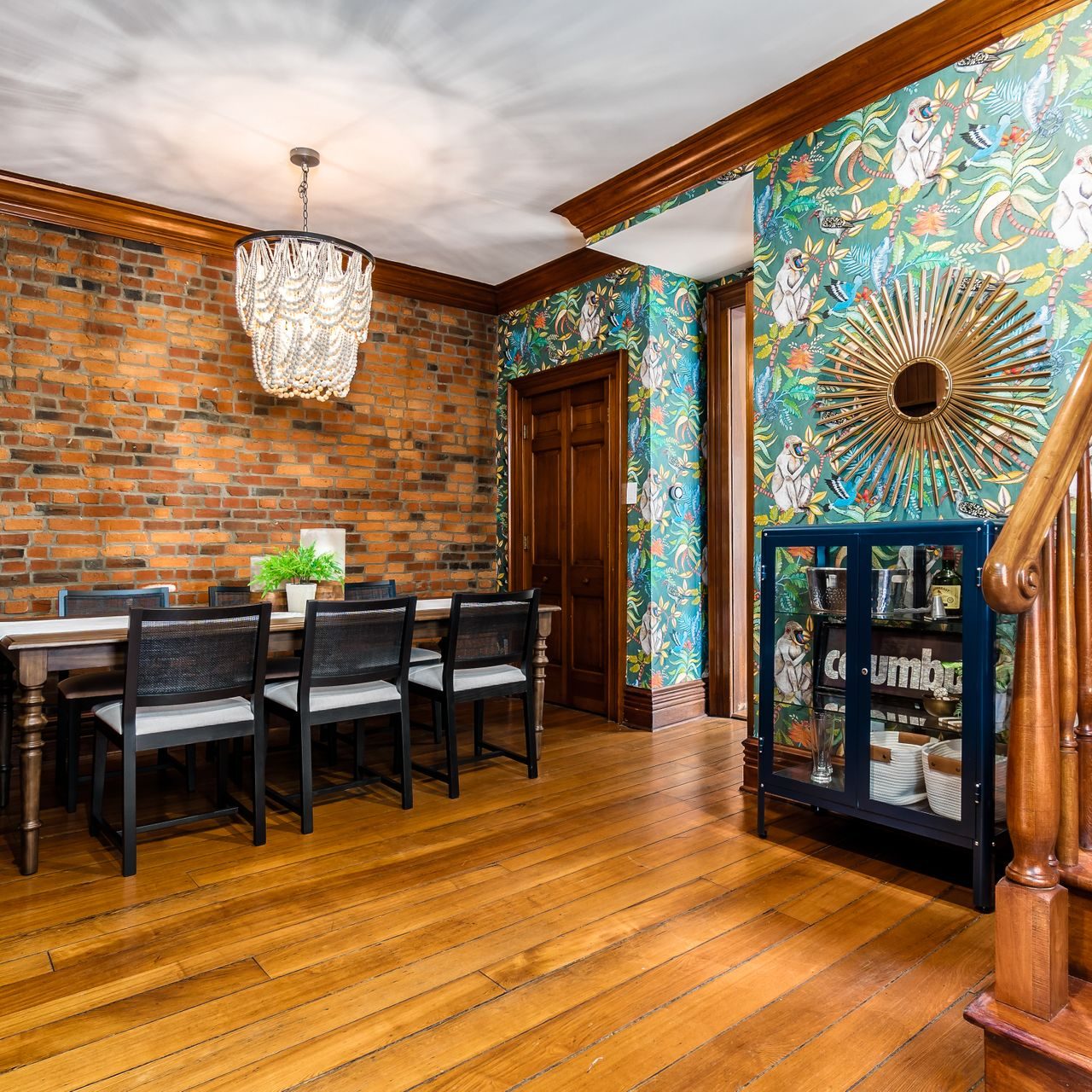 Wallpapered dining room with exposed brick, large chandelier, and professional home staging/interior design.