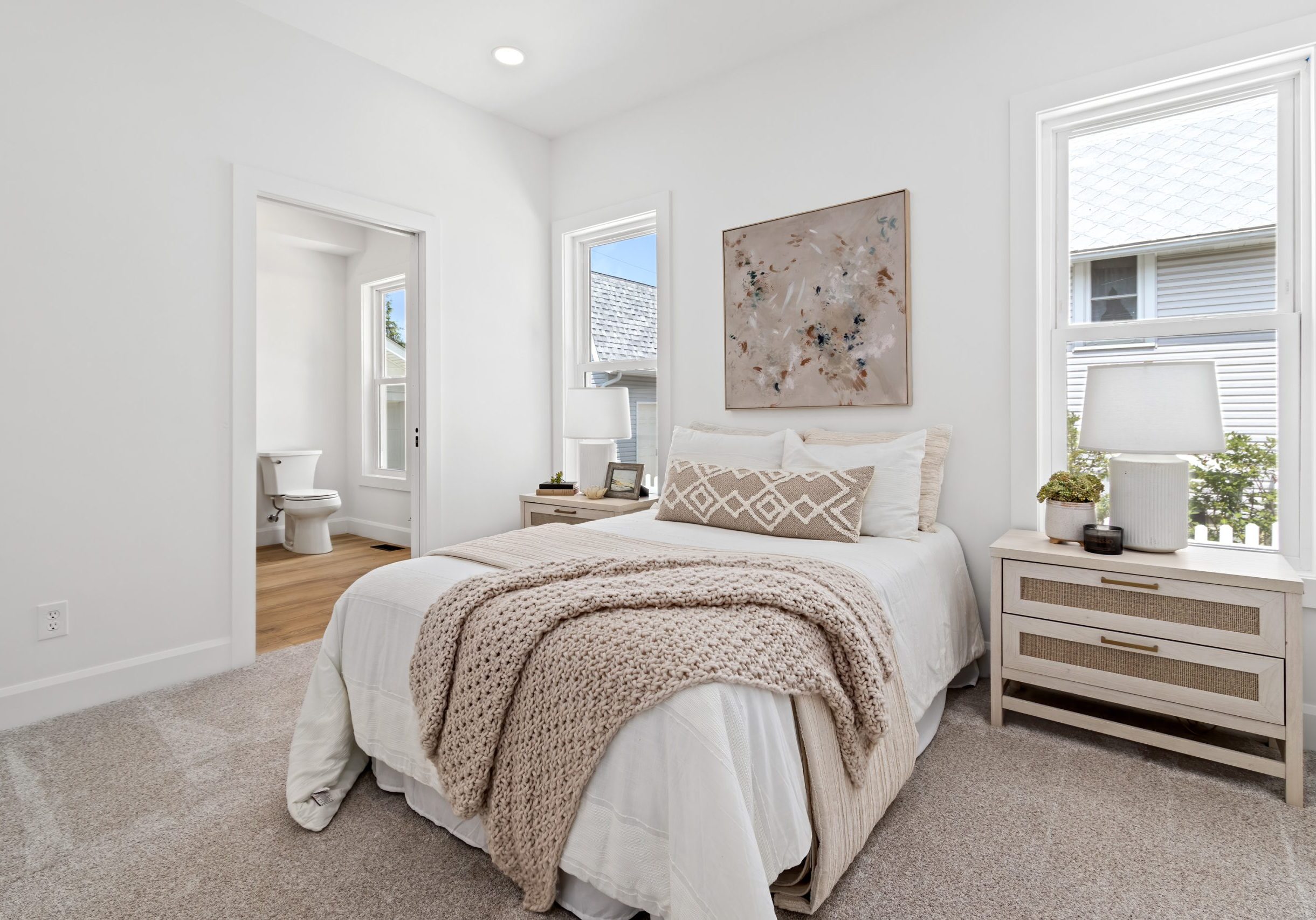 Primary bedroom in a recently remodeled Westerville, Ohio home featuring soft beige tones, abstract artwork, nightstands, and table lamps. Home was staged by interior design and staging company Jennifer Donahue Interior Design Inc.
