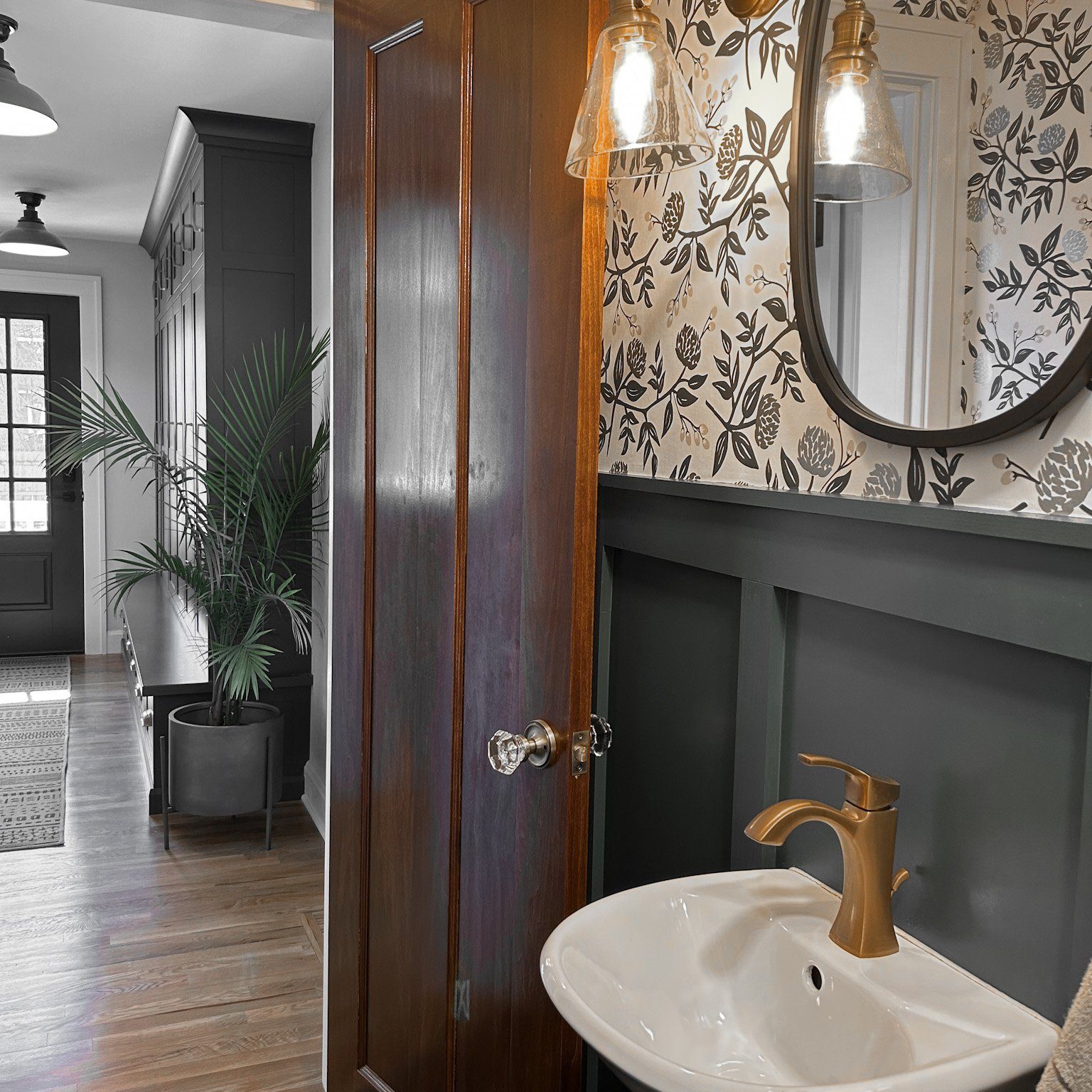 Classic bathroom with modern twist featuring ornate floral wallpaper, wainscoting and wall mounted mirror.