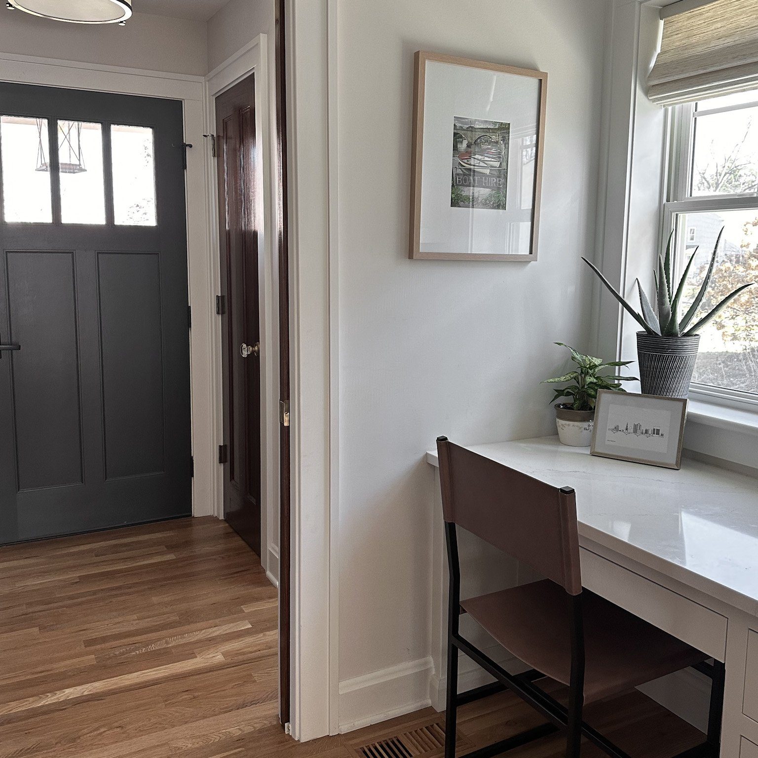 Entry way with small nook desk space styled with leather desk chair, potted plants and soft high end blinds.