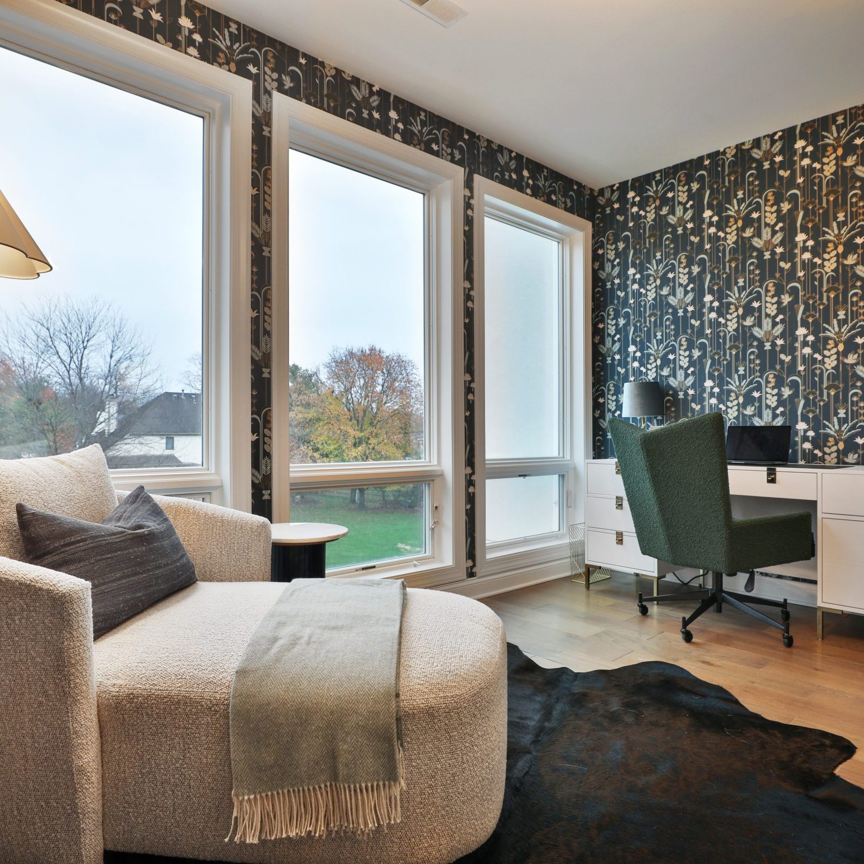 At home office space with ornate wallpaper, chaise lounge chair and warm lighting overlooking a country club gold course in luxury condo.