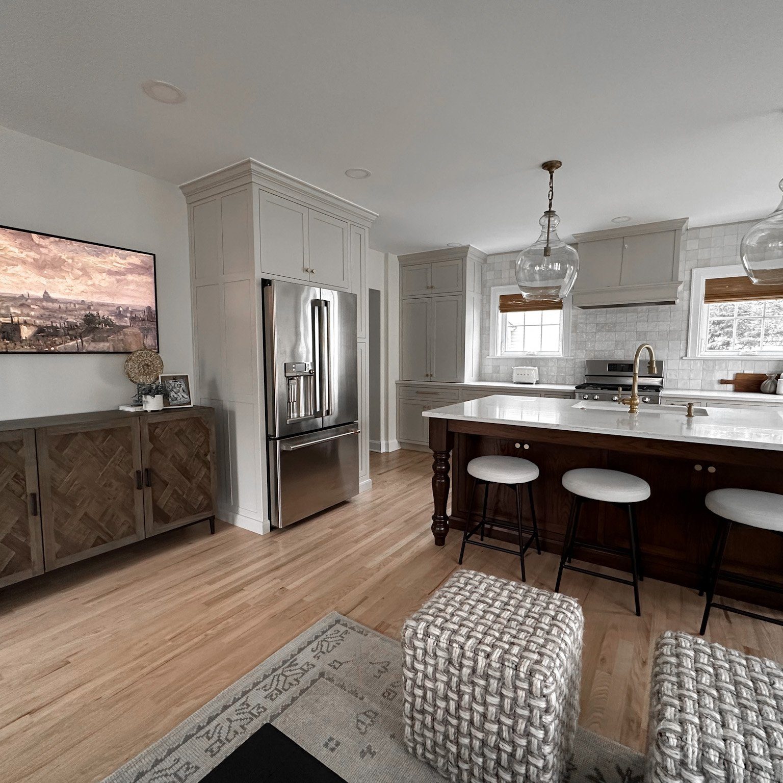 A view looking into the custom kitchen of a Columbus interior design client completed with a large wood console, stainless steel double door fridge and customer white countertop kitchen island.